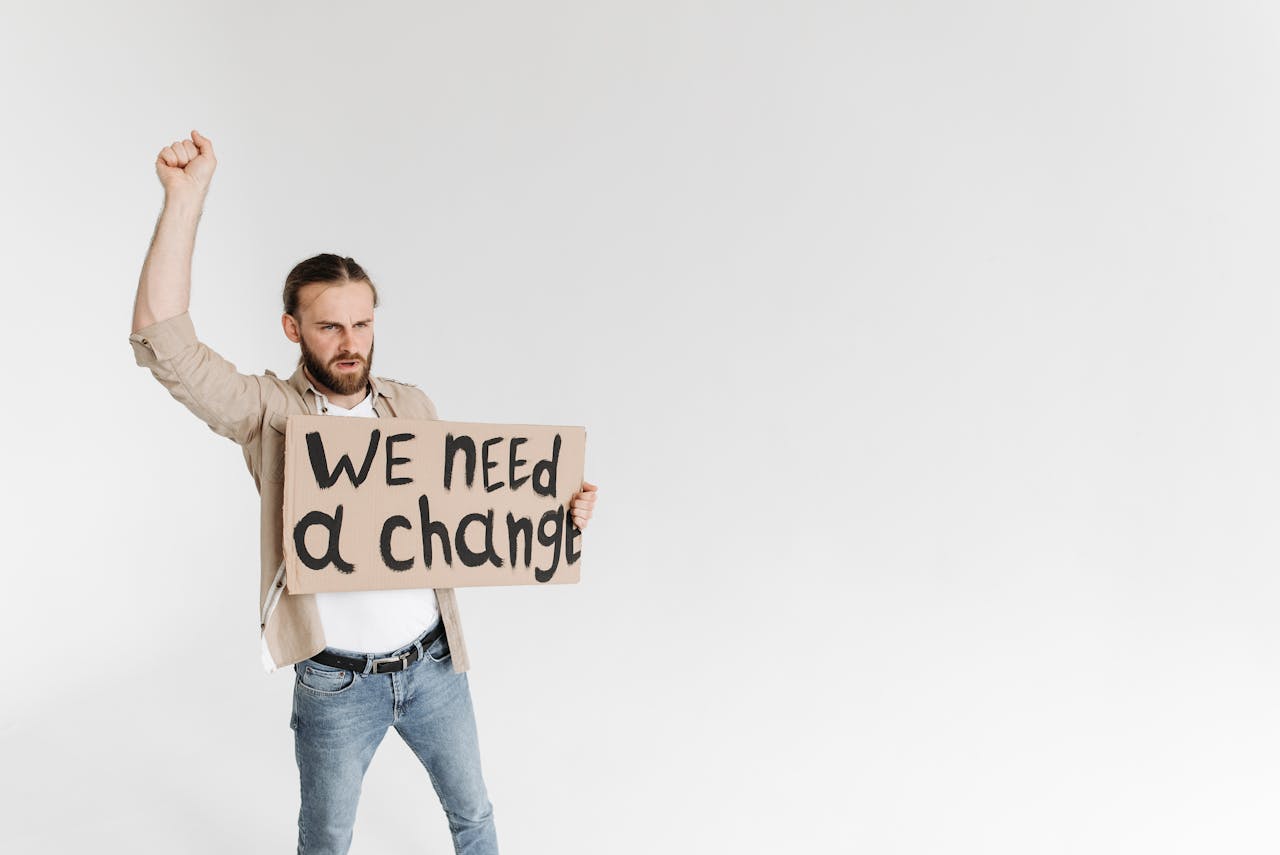 Man holding a 'We Need a Change' sign with raised fist, isolated background.