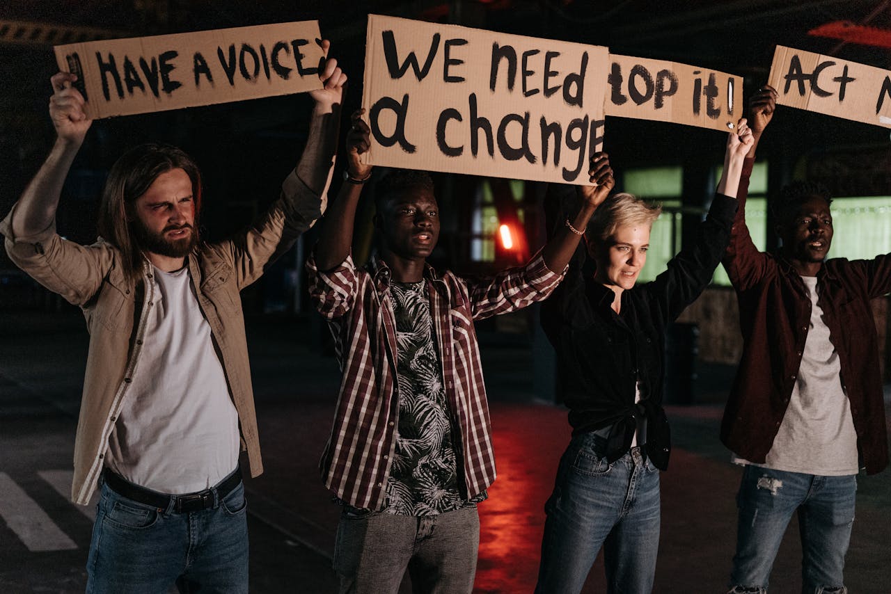 Diverse group holding protest signs demanding change, highlighted by night lighting.